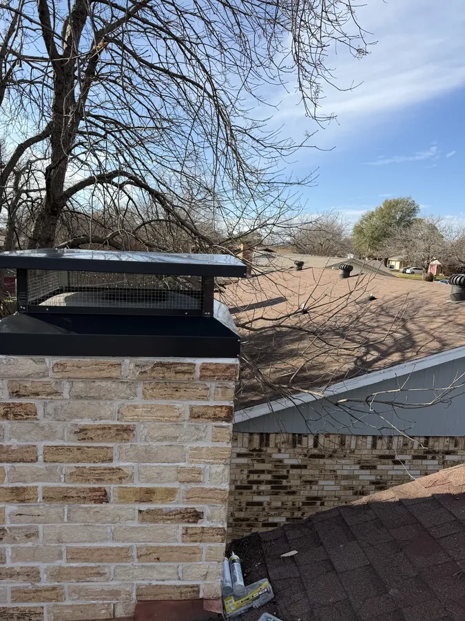 New black stainless chimney cap installed on a stone chimney