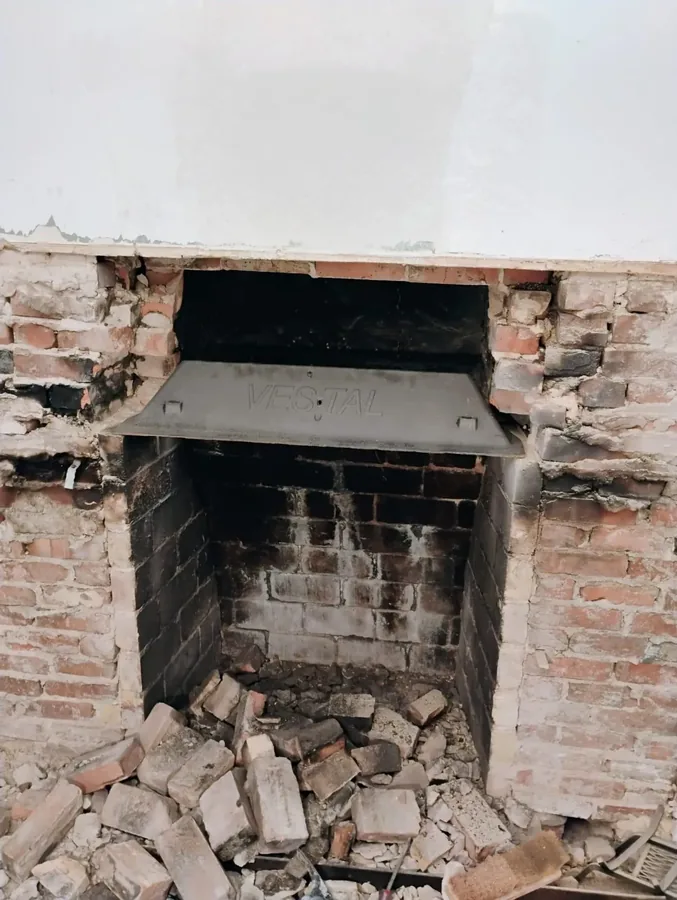 Fireplace opened up for repair, showing the exposed damper plate and brick rubble