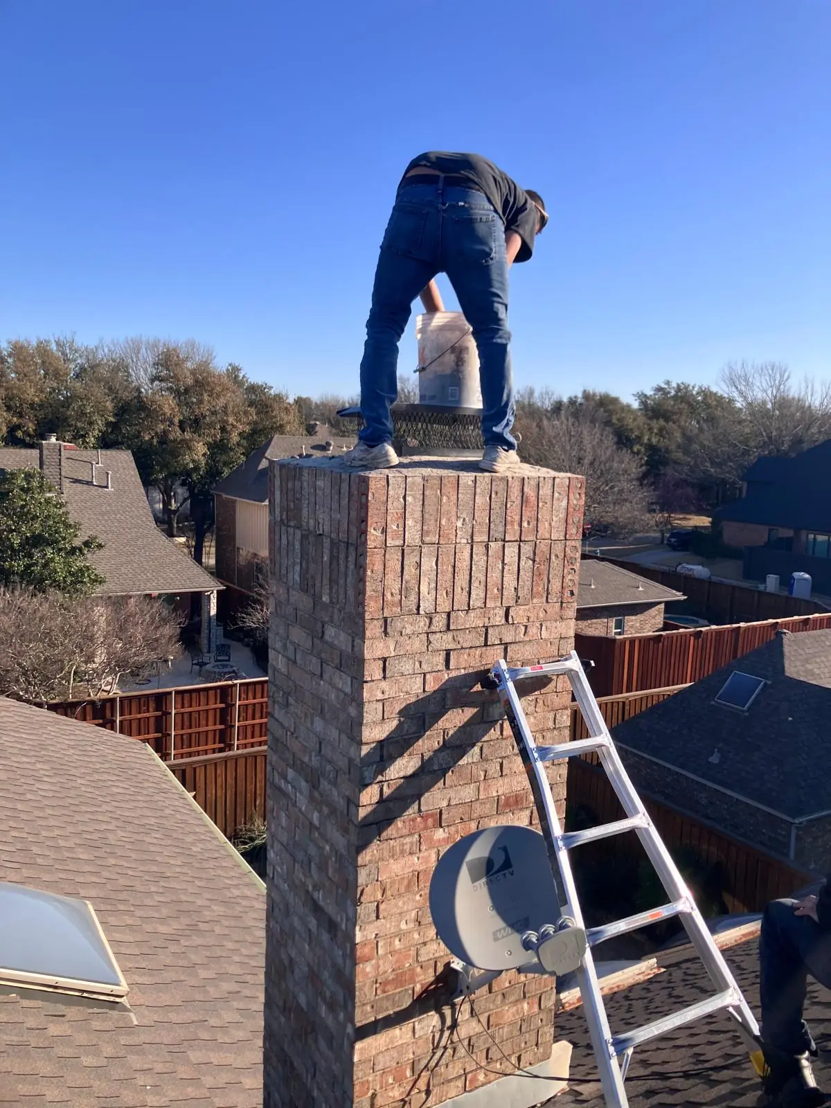Pure Chimney Sweep technician standing on a brick chimney against a clear blue sky