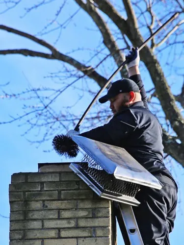 Technician installing a chimney cap from a ladder on the roof