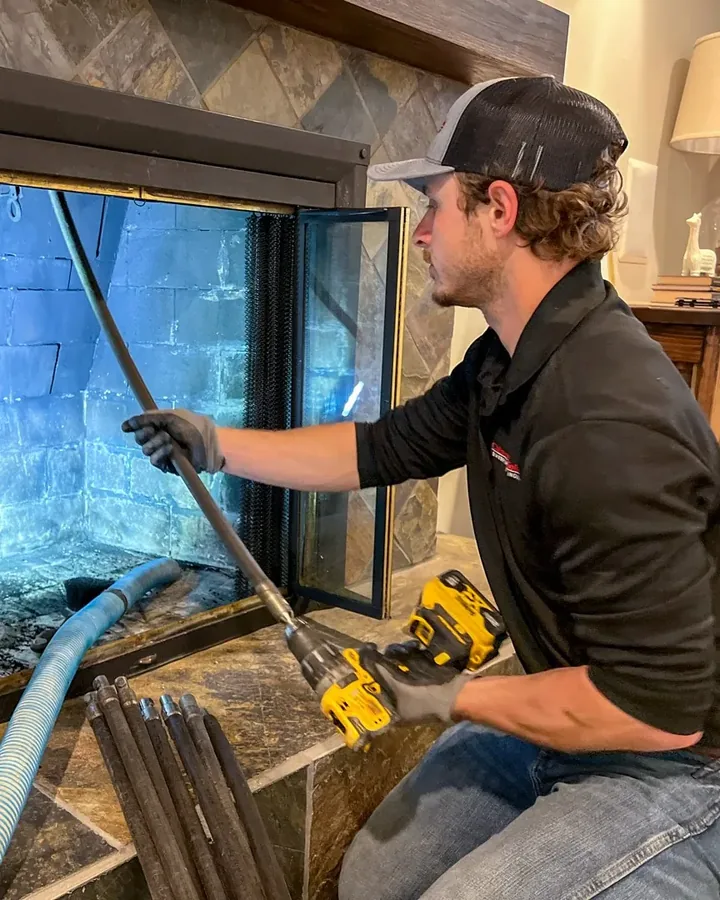 Technician using a drill-powered rod system to sweep a fireplace insert